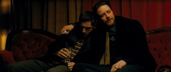 Movie still from “Filth” (2013), directed by Jon S. Baird – Two men sitting on a couch with a glass of wine; Medium shot, Low angle