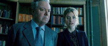 Movie still from “Filth” (2013), directed by Jon S. Baird – A man and a woman standing next to each other in front of a bookcase; Close Up shot, Low angle