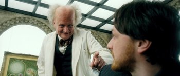 Movie still from “Filth” (2013), directed by Jon S. Baird – A man in a white jacket is talking to another man in a black tie; Medium shot, Over the shoulder angle