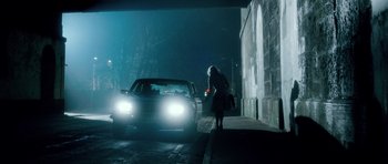 Movie still from “Filth” (2013), directed by Jon S. Baird – A woman standing on the side of a road next to a car; Wide shot, Over the shoulder angle