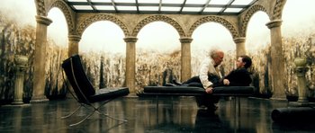 Movie still from “Filth” (2013), directed by Jon S. Baird – A man sitting on top of a bed in front of a painting; Wide shot, High angle