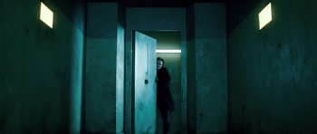 Movie still from “Filth” (2013), directed by Jon S. Baird – A woman standing in a doorway in a dark room; Wide shot, Low angle