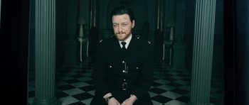 Movie still from “Filth” (2013), directed by Jon S. Baird – A man in a uniform sitting in a room; Medium shot, High angle