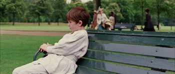 Movie still from “Finding Neverland” (2004), directed by Marc Forster – A boy sitting on top of a wooden park bench; Medium shot, Over the shoulder angle