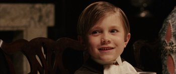 Movie still from “Finding Neverland” (2004), directed by Marc Forster – A young boy sitting in a chair smiling for the camera; Close Up shot, High angle