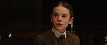 Movie still from “Finding Neverland” (2004), directed by Marc Forster – A boy in a suit and tie sitting in front of a chair; Close Up shot, Over the shoulder angle