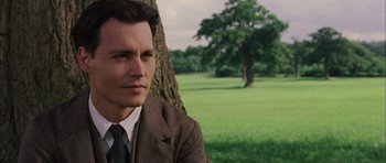 Movie still from “Finding Neverland” (2004), directed by Marc Forster – A man wearing a suit and tie sitting in front of a tree in a field; Close Up shot, Over the shoulder angle