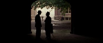 Movie still from “Finding Neverland” (2004), directed by Marc Forster – Two men standing under an archway on a sidewalk; Wide shot, High angle