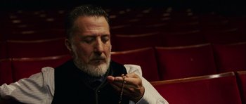 Movie still from “Finding Neverland” (2004), directed by Marc Forster – An older man is holding a rosary in a theater; Close Up shot, Low angle