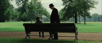 Movie still from “Finding Neverland” (2004), directed by Marc Forster – A man in a black suit and a woman in a black hat are sitting on a park bench; Wide shot, Over the shoulder angle