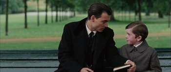 Movie still from “Finding Neverland” (2004), directed by Marc Forster – A man sitting on top of a bench reading a book; Close Up shot, Over the shoulder angle