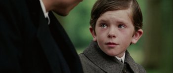 Movie still from “Finding Neverland” (2004), directed by Marc Forster – A young boy in a suit and tie looking at the camera; Close Up shot, Over the shoulder angle