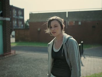Movie still from “Fish Tank” (2009), directed by Andrea Arnold – A young woman is standing on the sidewalk; Medium shot, Low angle