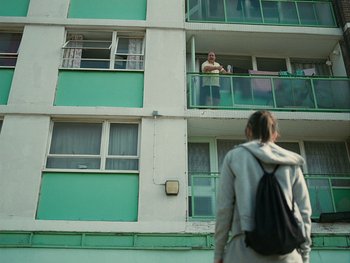 Movie still from “Fish Tank” (2009), directed by Andrea Arnold – A woman standing on a balcony looking out of a window; Wide shot, Low angle