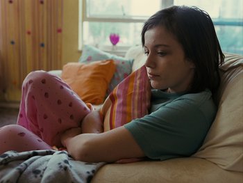 Movie still from “Fish Tank” (2009), directed by Andrea Arnold – A woman laying on a bed looking at a pink pillow; Medium shot, High angle