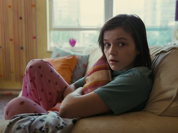 Movie still from “Fish Tank” (2009), directed by Andrea Arnold – A young woman sitting on a couch with her legs crossed; Medium shot, High angle