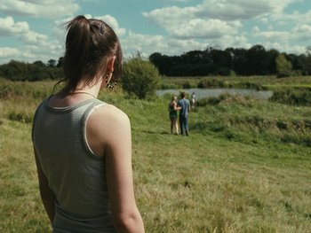 Movie still from “Fish Tank” (2009), directed by Andrea Arnold – A woman standing in a field looking at a group of people; Wide shot, Over the shoulder angle