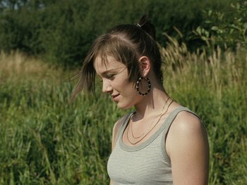 Movie still from “Fish Tank” (2009), directed by Andrea Arnold – A young woman with long brown hair wearing a silver tank top; Close Up shot, Over the shoulder angle