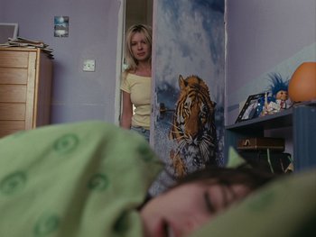 Movie still from “Fish Tank” (2009), directed by Andrea Arnold – A woman standing next to a child sleeping in a bed; Medium shot, Over the shoulder angle