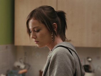 Movie still from “Fish Tank” (2009), directed by Andrea Arnold – A woman with a ponytail is standing in a kitchen; Close Up shot, Over the shoulder angle