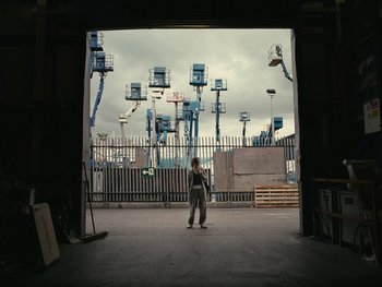 Movie still from “Fish Tank” (2009), directed by Andrea Arnold – A man standing on a skateboard in an empty parking lot; Extreme Wide shot, Low angle