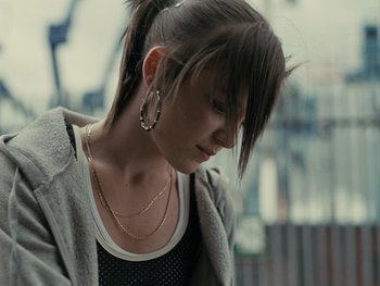 Movie still from “Fish Tank” (2009), directed by Andrea Arnold – A young woman with long brown hair wearing a black top; Close Up shot, Over the shoulder angle