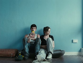 Movie still from “Fish Tank” (2009), directed by Andrea Arnold – A man and a woman sitting next to each other on the ground; Wide shot, Low angle