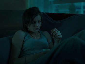 Movie still from “Fish Tank” (2009), directed by Andrea Arnold – A woman sitting on a couch holding a coffee mug; Medium shot, High angle