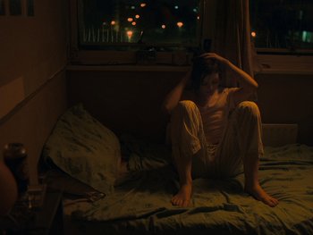Movie still from “Fish Tank” (2009), directed by Andrea Arnold – A woman sitting on a bed in the dark; Medium shot, High angle