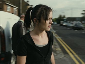 Movie still from “Fish Tank” (2009), directed by Andrea Arnold – A woman walking down a street with a ponytail; Close Up shot, Over the shoulder angle