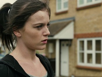 Movie still from “Fish Tank” (2009), directed by Andrea Arnold – A woman standing in front of a brick building; Close Up shot, Over the shoulder angle