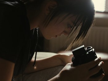 Movie still from “Fish Tank” (2009), directed by Andrea Arnold – A woman is looking at a camera on a bed; Close Up shot, High angle