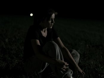 Movie still from “Fish Tank” (2009), directed by Andrea Arnold – A woman sitting in the grass at night; Medium shot, High angle