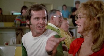 Movie still from “Five Easy Pieces” (1970), directed by Bob Rafelson – A man and a woman are sitting in front of other people; Close Up shot, Over the shoulder angle