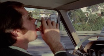 Movie still from “Five Easy Pieces” (1970), directed by Bob Rafelson – A man in a car holding a soda and drinking; Close Up shot, Over the shoulder angle