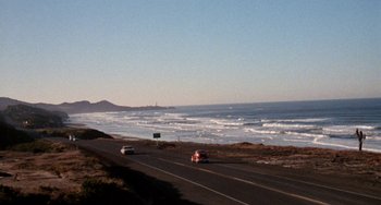 Movie still from “Five Easy Pieces” (1970), directed by Bob Rafelson – Cars driving down a road near the ocean on a sunny day; Extreme Wide shot, High angle
