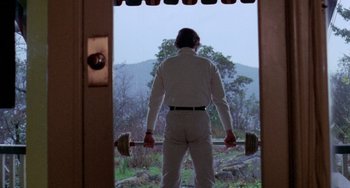 Movie still from “Five Easy Pieces” (1970), directed by Bob Rafelson – A man holding a barbell while standing in front of a window; Wide shot, Low angle