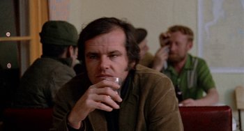 Movie still from “Five Easy Pieces” (1970), directed by Bob Rafelson – A man sitting in front of other men drinking a beverage; Close Up shot, Over the shoulder angle