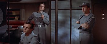 Movie still from “Forbidden Planet” (1956), directed by Fred M. Wilcox – A man holding a microphone while standing next to a window; Medium shot, Low angle