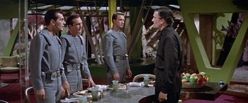 Movie still from “Forbidden Planet” (1956), directed by Fred M. Wilcox – A group of men standing next to each other at a table; Medium shot, Over the shoulder angle