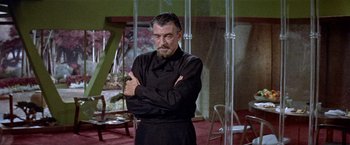 Movie still from “Forbidden Planet” (1956), directed by Fred M. Wilcox – A man in a black shirt is standing with his arms crossed; Medium shot, Over the shoulder angle