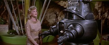 Movie still from “Forbidden Planet” (1956), directed by Fred M. Wilcox – A woman standing next to a robot in a room; Medium shot, Low angle