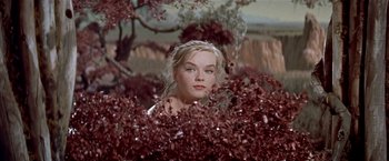 Movie still from “Forbidden Planet” (1956), directed by Fred M. Wilcox – A beautiful young woman standing next to a bunch of red flowers; Close Up shot, Low angle