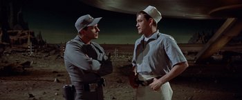 Movie still from “Forbidden Planet” (1956), directed by Fred M. Wilcox – Two men standing next to each other on a dirt field; Medium shot, Low angle