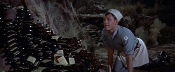 Movie still from “Forbidden Planet” (1956), directed by Fred M. Wilcox – A man is looking at a pile of beer bottles; Medium shot, High angle
