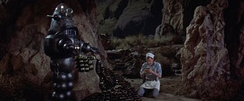 Movie still from “Forbidden Planet” (1956), directed by Fred M. Wilcox – A man kneeling on the ground in front of a robot; Wide shot, High angle