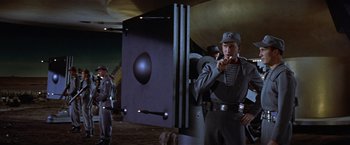 Movie still from “Forbidden Planet” (1956), directed by Fred M. Wilcox – A group of men standing next to each other in a room; Medium shot, Low angle