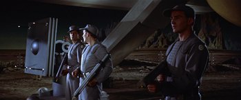 Movie still from “Forbidden Planet” (1956), directed by Fred M. Wilcox – A group of men standing next to each other holding guns; Medium shot, Low angle