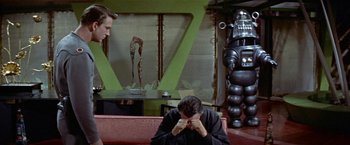 Movie still from “Forbidden Planet” (1956), directed by Fred M. Wilcox – Two men sitting on a couch in front of a robot; Medium shot, Over the shoulder angle