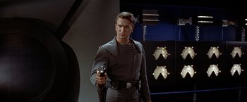 Movie still from “Forbidden Planet” (1956), directed by Fred M. Wilcox – A man holding a gun while standing next to a wall; Medium shot, Over the shoulder angle